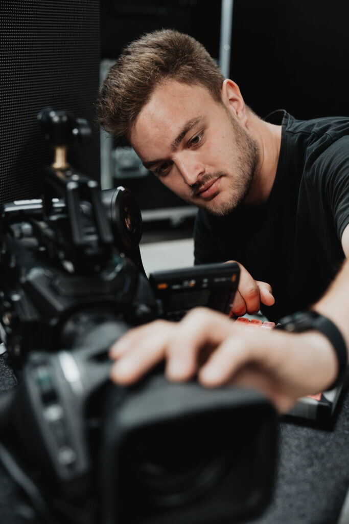 Videotechniker richtet eine professionelle Kamera mit Monitor für einen Livestream ein; er hat die Hände am Bedienfeld am Objektiv