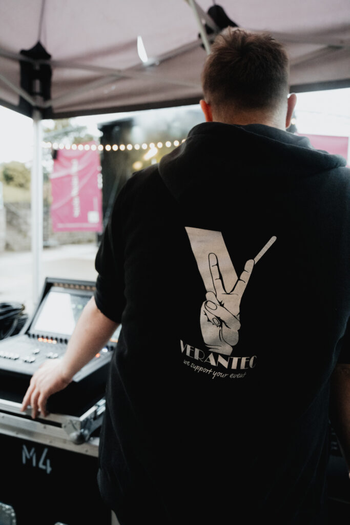 Rückenansicht eines Technikers von Verantec; er betreut das FOH bei einem Corporate Event mit einem Mischpult das auf einem Flightcase steht