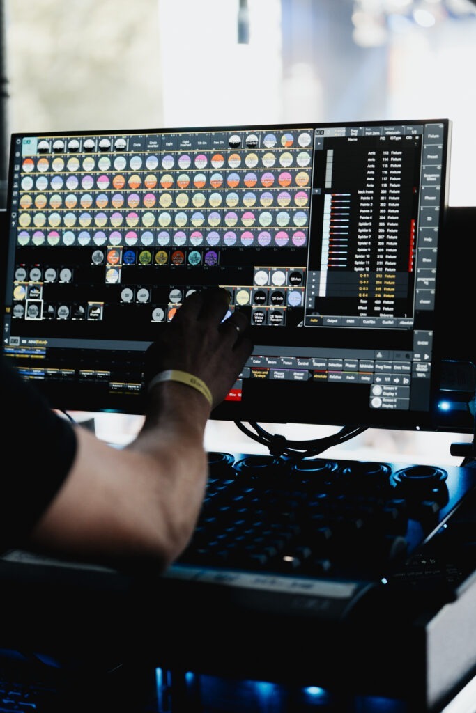 Lichtsteuerung am FOH: ein Eventtechniker bedient mit seiner rechten Hand eine Show-Software auf großem Monitor mit Presets und DMX-Kanälen