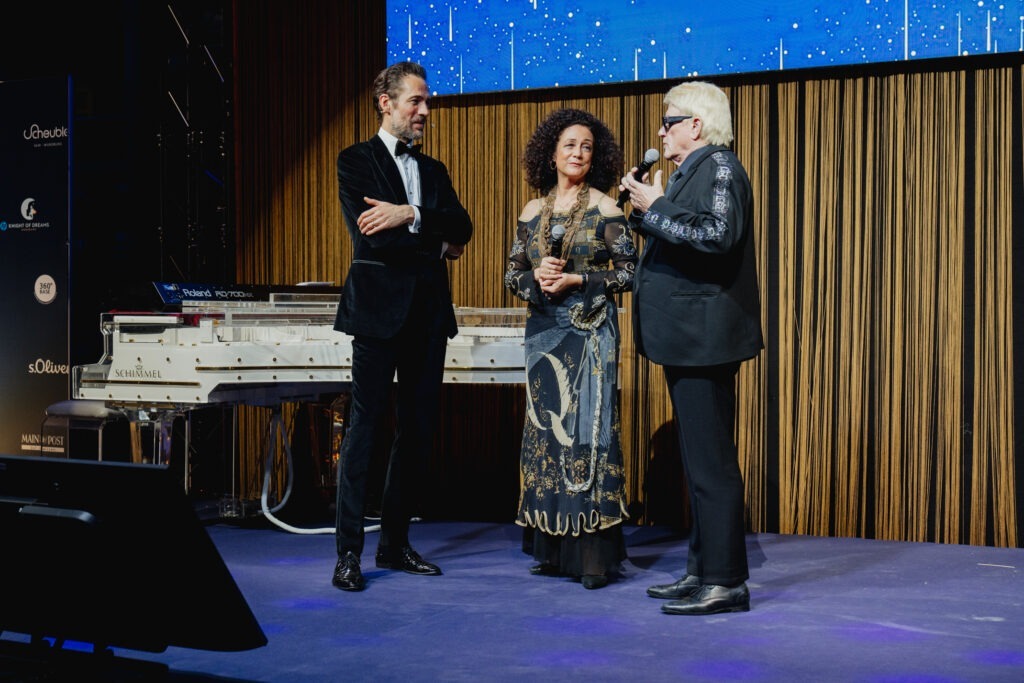 Der Schlagermusiker Heino, der Moderator Alexander Mazza und die Schauspielerin Barbara Wussow auf der Bühne eines Corporate-Events. Heino spricht ins Mikrofon.